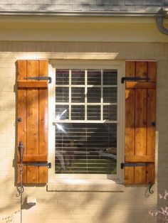 an open window with wooden shutters on the side of a house in front of a tree