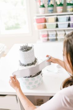 a woman is decorating a cake with white frosting and silver decorations on it