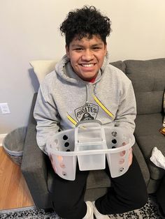 a young man sitting on a couch holding a plastic container in his hands and smiling at the camera