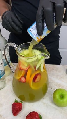 a person in black gloves pours liquid into a pitcher filled with fruit