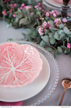 a pink grapefruit sitting on top of a white plate next to some flowers