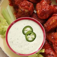 a plate with chicken wings and dip on it, surrounded by celery sticks