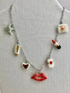 Vintage-themed charm necklace on a gold bar chain; all the charms are sculpted from a fine white porcelain clay and painted by hand to have charming details. Back and front sides are painted. Since they are made from porcelain and glossed with a clear glaze, each charm is smooth and soft to the touch.  Each charm is attached to a small, gold jump ring that can be attached to a necklace chain. Small charms featured: Blue-green Sea Star, Love Letter w/ gold highlights, Red Lipstick with gold band, Red lips, Slipper with gold heart, Gold Heart (gold raindrops on one side, gold heart on the other), Lucky Strikes pack. Bought individually, your charm(s) will come with a thin, black velvet ribbon to tie as a choker necklace. You can also buy a 7-charm necklace that comes with a gold bar necklace Artsy White Jewelry For Gifts, White Vintage Charm Necklaces As Gift, Cute Red Handmade Charm Necklace, Playful Handmade Gold Charm Necklaces, Dainty Handmade Red Charm Necklaces, Whimsical White Charm Necklaces, White Ceramic Jewelry As A Gift, Whimsical White Charm Necklace, Red Vintage Charm Necklace For Gift