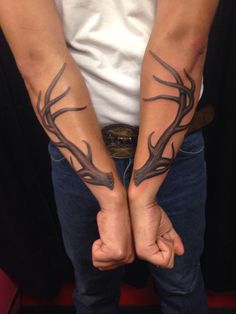 two people holding hands with tattoos on their arms and the other hand is covered by antlers