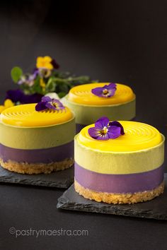 three small cakes with flowers on top of each one, sitting on slates next to each other