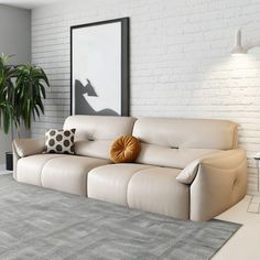 a living room with a couch, table and potted plant on the floor in front of a white brick wall