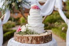 a white wedding cake sitting on top of a wooden table next to a tree stump