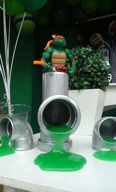 there is a green substance on the table next to plastic cups and vases with balloons in the background