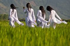 four women in white are walking through the grass