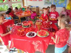 a group of children standing around a table with plates of fruit and watermelon