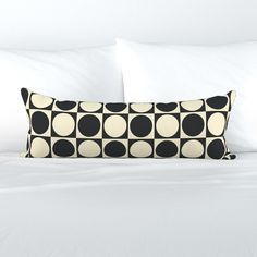 a black and white pillow sitting on top of a bed next to a pair of pillows