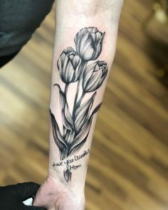 a black and white flower tattoo on the left inner arm with an inscription above it