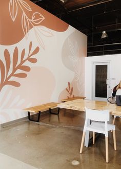 a woman sitting at a table in front of a wall with flowers painted on it