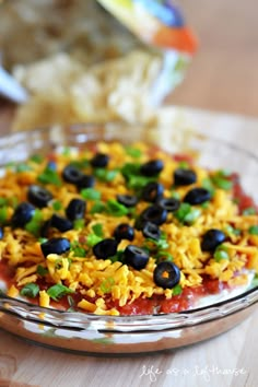 a dish with rice, black olives and green peppers on it sitting on a wooden table