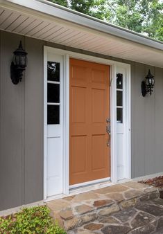 the front door of a house with two lights on each side and an orange door