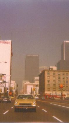 a yellow car driving down a city street next to tall buildings and traffic lights in the distance