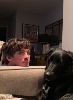 a man sitting on a couch next to a black dog