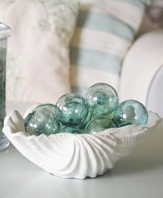 a bowl filled with green glass balls on top of a table next to a vase