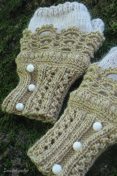 two knitted mittens sitting on top of green grass next to each other with white buttons