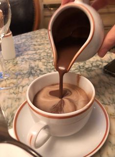 someone pouring chocolate into a cup on top of a saucer