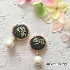 two earrings with flowers and pearls are on a table next to some pink flowers in the background