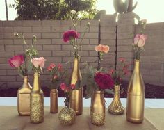 six gold vases with flowers in them sitting on a table next to a brick wall