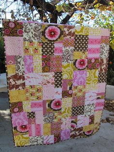 a patchwork quilt hanging from a tree in front of a building with flowers on it