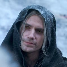 a man with long hair and yellow eyes wearing a hoodie looking at the camera