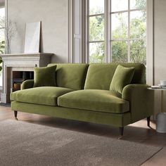 a green couch sitting in front of a window next to a rug on top of a wooden floor