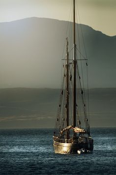 a sailboat in the ocean with mountains in the background