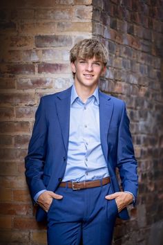 a young man in a blue suit standing next to a brick wall with his hands on his hips