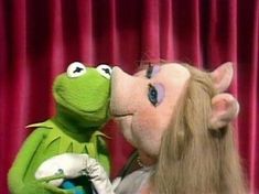 kermie and miss piggy kissing each other in front of a red curtain