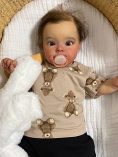 a baby with a pacifier in its mouth laying on a bed next to a stuffed animal