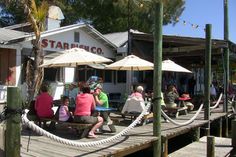 people sitting at tables on a dock with umbrellas in front of the restaurant and outside dining area