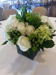 a vase filled with white flowers and greenery on top of a table in a room