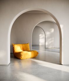 a yellow chair sitting in the middle of a room next to a white wall and arched doorway