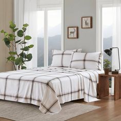 a bed with white and black plaid sheets in a room next to a plant on a table