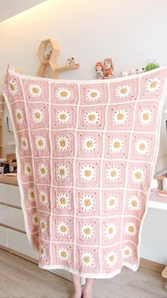 a woman is holding up a pink crocheted blanket in the middle of a kitchen