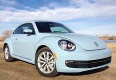 a light blue volkswagen beetle parked in the dirt