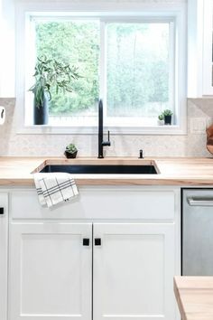 a kitchen with white cabinets and wooden counter tops next to a window that has a potted plant on it