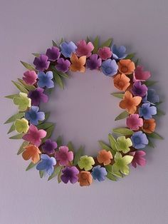 a wreath made out of paper flowers is hanging on the wall in front of a purple wall