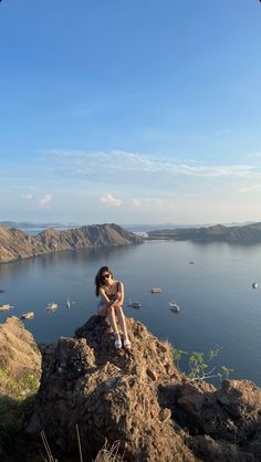 a woman sitting on top of a rock next to the ocean