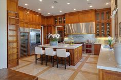 a large kitchen with wooden cabinets and marble counter tops, along with an island in the middle