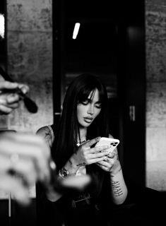 a black and white photo of a woman looking at her cell phone while another person holds something in their hand