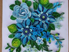 a card with blue flowers and green leaves on white paper in the shape of a bouquet