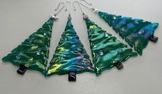 four green and blue glass christmas trees hanging from silver earwires on a white surface