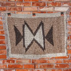 an arrow rug hanging on the side of a brick wall with two black arrows pointing in opposite directions