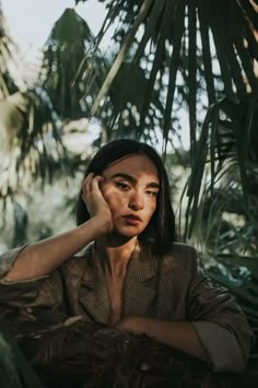 a woman sitting in the palm trees with her hand on her head and looking off into the distance