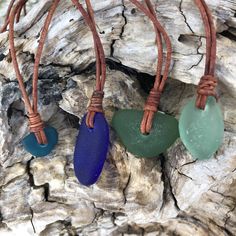 three pieces of sea glass are hanging from a cord on a piece of driftwood