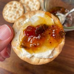 a hand holding a cracker with jelly and cream on it next to crackers